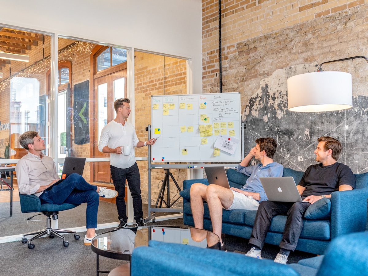 A team in a brick-walled studio planning on a whiteboard with sticky notes and laptops