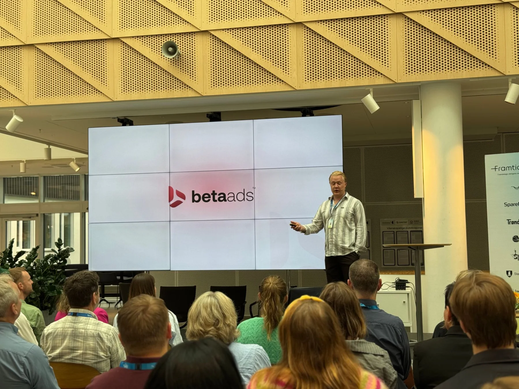 Andreas Myraune på scenen på Framtidsfredag foran en storskjerm med Beta Ads-logoen, publikum i forgrunnen
